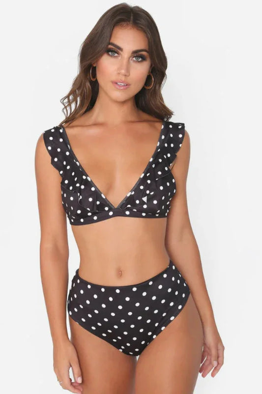 Woman wearing a black and white polka dot bikini with ruffled trim and high-waisted bottoms.