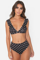Woman wearing a black and white polka dot bikini with ruffled trim and high-waisted bottoms.