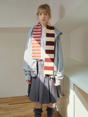 Model wearing a white lace camisole, grey zip-up hoodie, grey pleated skirt, and a striped scarf with pink and brown stripes.