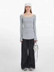 Front view of a woman wearing a grey long-sleeve ribbed knit top with bell sleeves and dark wash wide-leg jeans, holding a silver handbag.