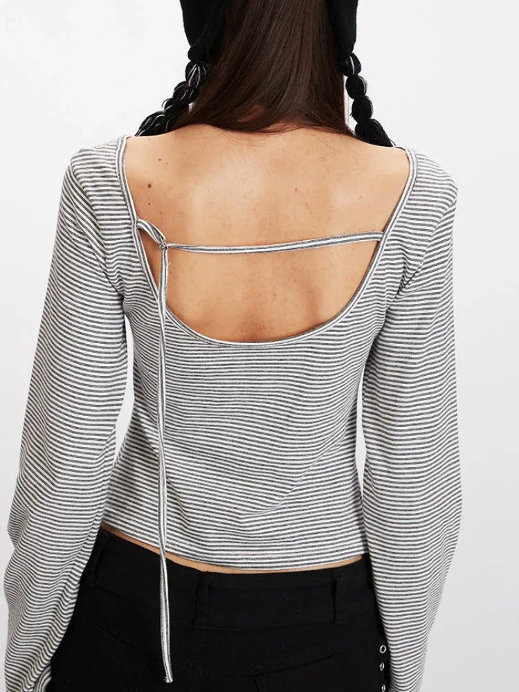 Close-up back view of a model wearing a grey and white striped long-sleeved cropped top with an open back and a tie detail.