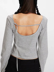 Close-up back view of a model wearing a grey and white striped long-sleeved cropped top with an open back and a tie detail.