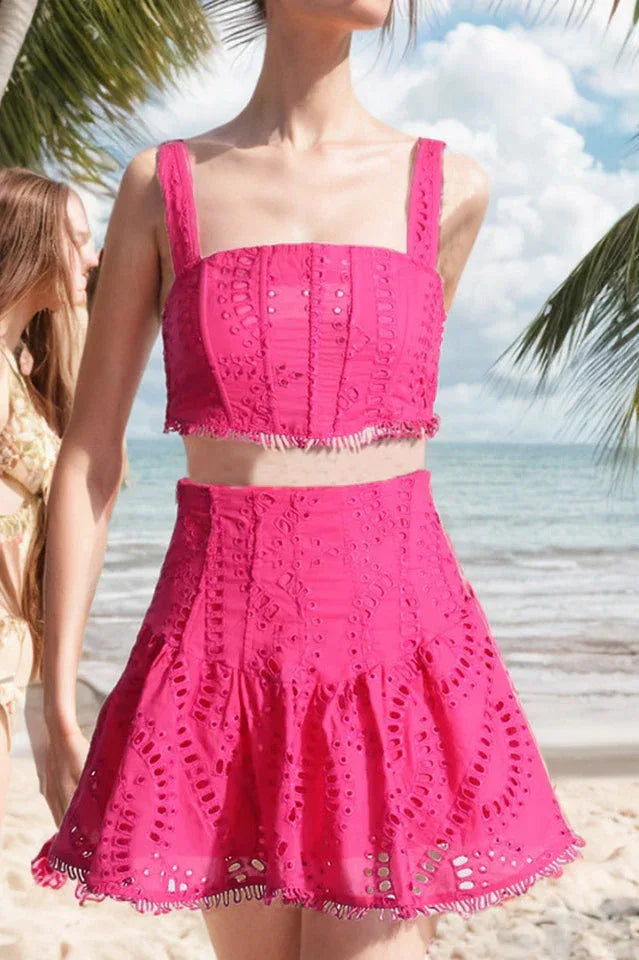 Woman wearing a bright pink embroidered eyelet crop top and flared skirt set on a beach.