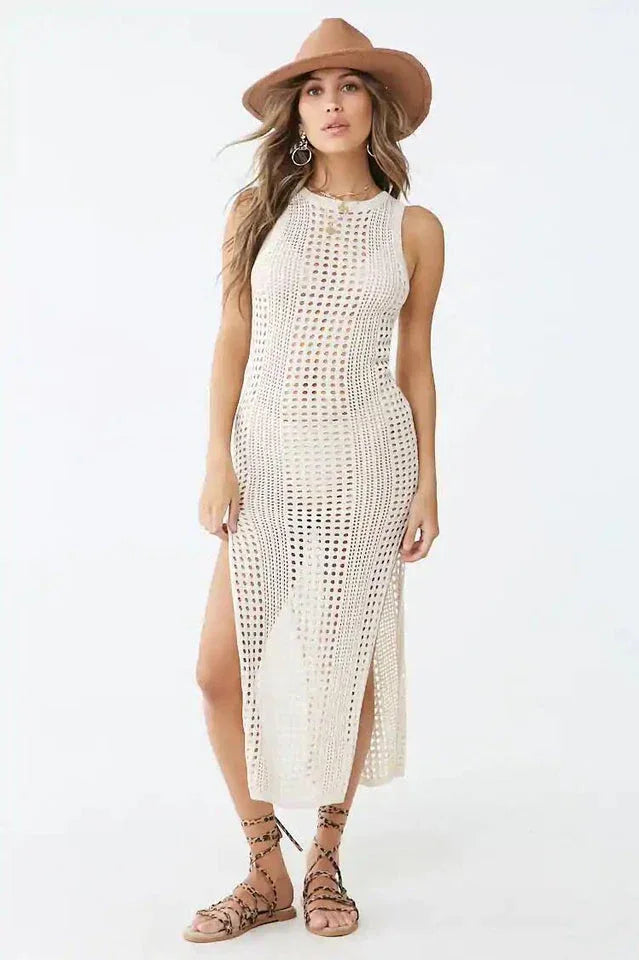 Woman wearing a cream crocheted knit sleeveless maxi dress with a high slit and a wide-brim hat.