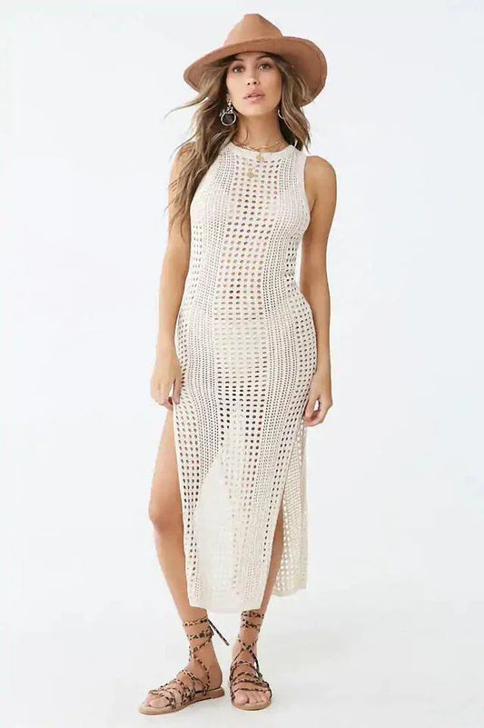 Woman wearing a cream crocheted knit sleeveless maxi dress with a high slit and a wide-brim hat.
