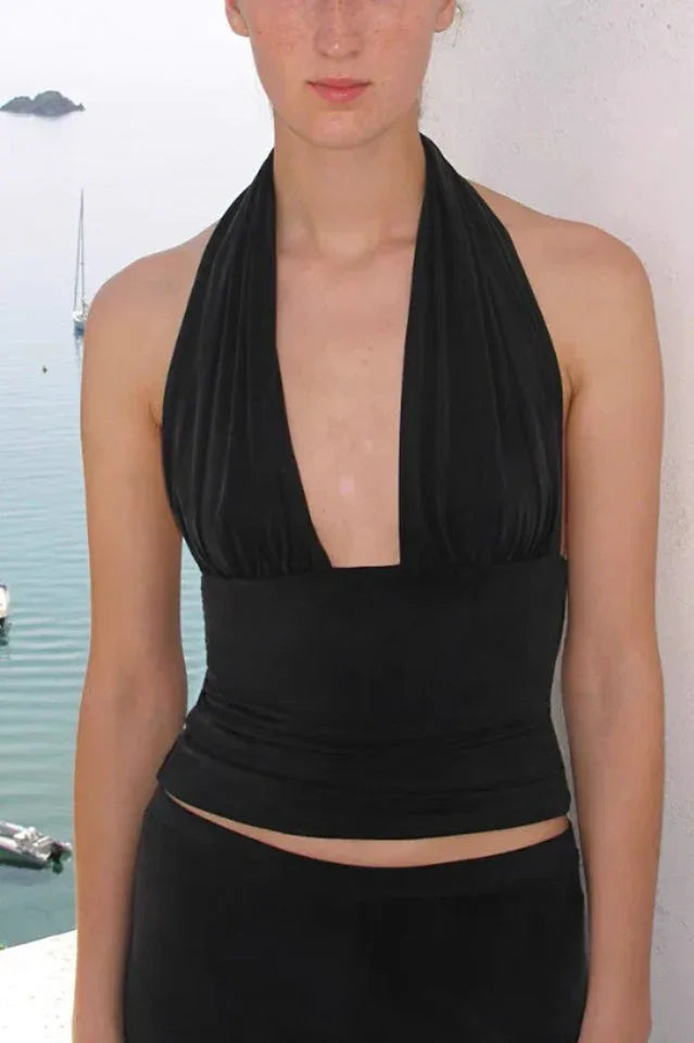 Woman wearing a black halter neck crop top with a deep V-neckline and matching black pants.