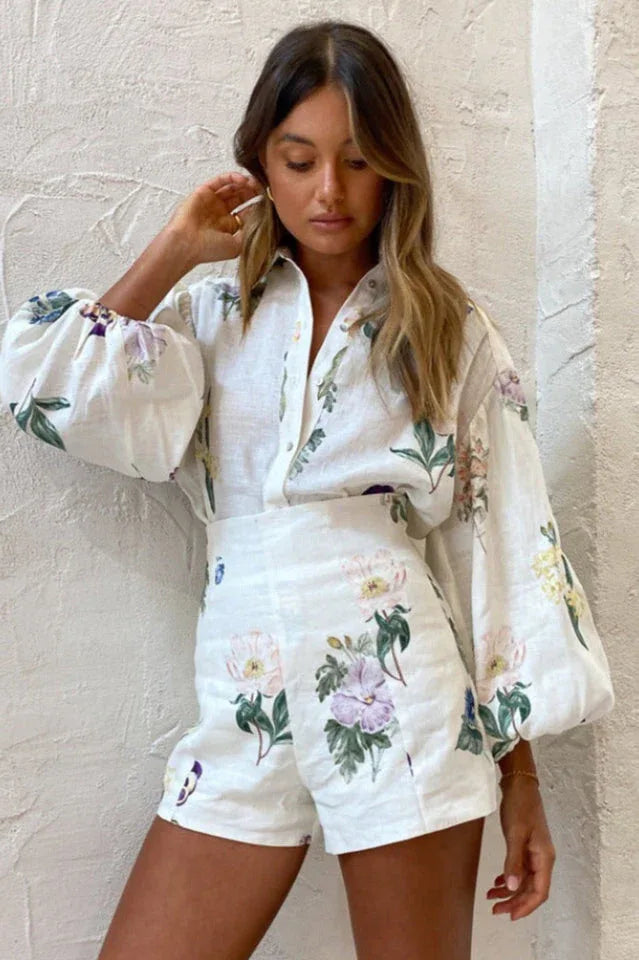 Close-up of a woman wearing a white floral print button-down shirt with puffed sleeves and matching high-waisted shorts