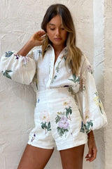 Close-up of a woman wearing a white floral print button-down shirt with puffed sleeves and matching high-waisted shorts
