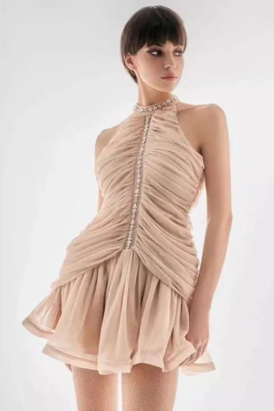 woman in a beige ruched halter neck mini dress with embellished neckline