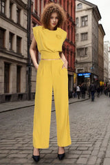 Woman wearing a yellow two-piece set with a cropped top and wide-leg pants, standing in a city street.