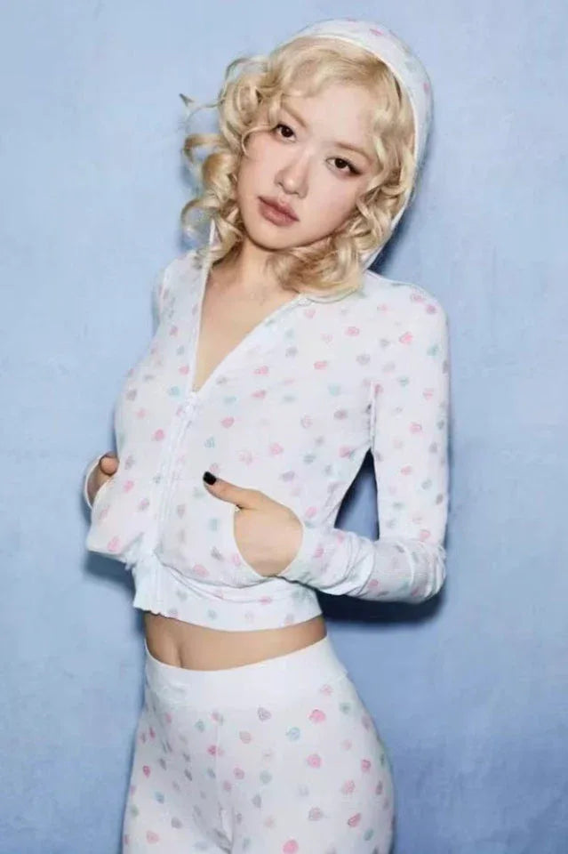 Woman with blonde curly hair wearing a white cropped hoodie with heart prints and matching bottoms.
