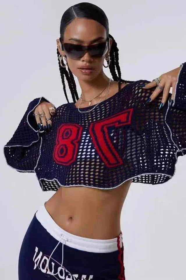 Woman wearing a navy blue cropped open-knit sweater with red appliquéd numbers and white trim, styled with sunglasses and jewelry.