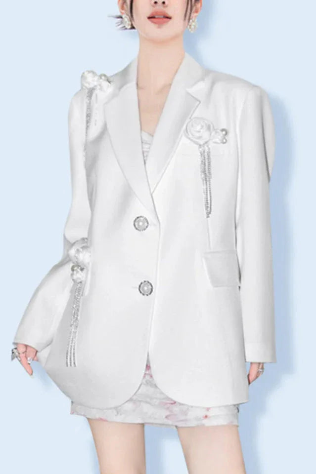 Woman wearing a white oversized blazer with floral embellishments and tassel detailing.