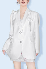 Woman wearing a white oversized blazer with floral embellishments and tassel detailing.