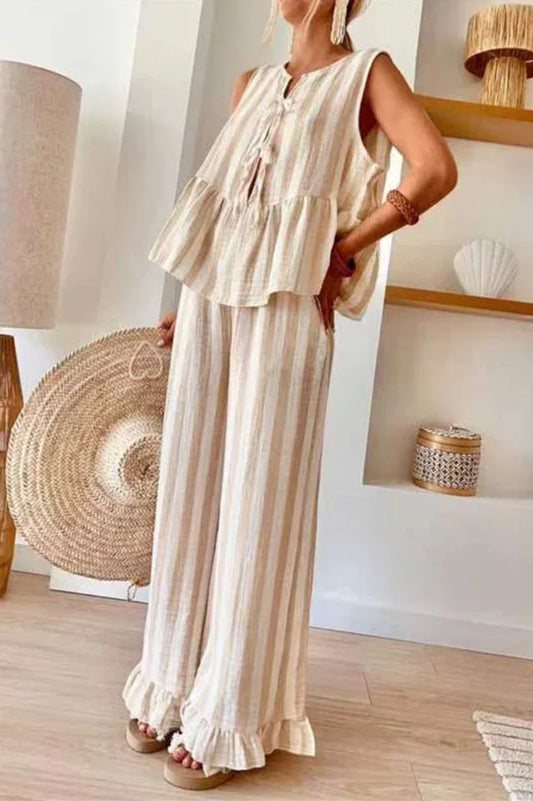 Woman wearing a beige and white striped sleeveless tiered top with tie-front closure and wide leg pants with ruffled hems.