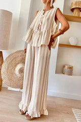 Woman wearing a beige and white striped sleeveless tiered top with tie-front closure and wide leg pants with ruffled hems.