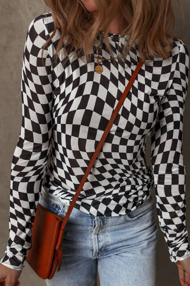 Close-up front view of a woman wearing a black and white checkerboard long-sleeved mesh top, blue jeans, and a brown crossbody bag.