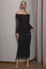 Woman wearing a black off-the-shoulder floor-length dress with sparkling embellishments, standing against a neutral backdrop.
