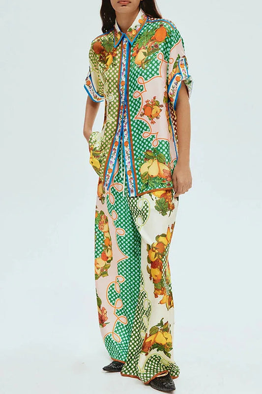 Model wearing a fruit print pajama set with a collared short-sleeve top and wide-leg pants.