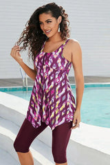 Woman wearing a purple, pink, and yellow abstract print tankini with burgundy capri leggings by a pool, showing the front.