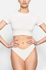 Model wearing a white cropped t-shirt and matching underwear, hands on hips
