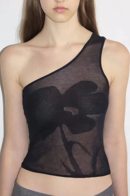 Close-up of a woman wearing a black asymmetrical sheer knit top with a floral appliqué.