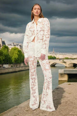 Woman wearing a sheer white lace button-down shirt and flare leg pants standing by a river in Paris.