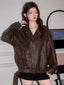 Woman wearing a brown faux leather moto jacket with a grey crop top and black shorts.