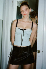 A young woman stands in a doorway wearing a light blue cropped top with black trim and a black mini skirt.