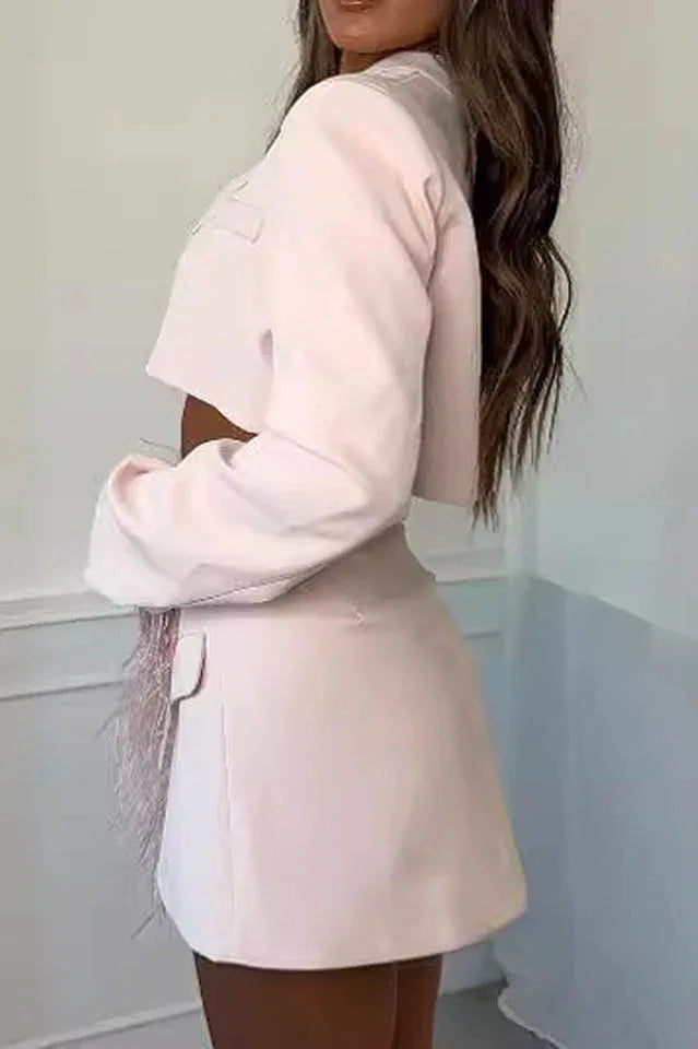 Back view of a woman wearing a pink cropped blazer and asymmetrical skirt with feather trim