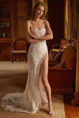 A woman in a white, beaded mermaid wedding dress with a high slit and train, standing with her arms crossed.