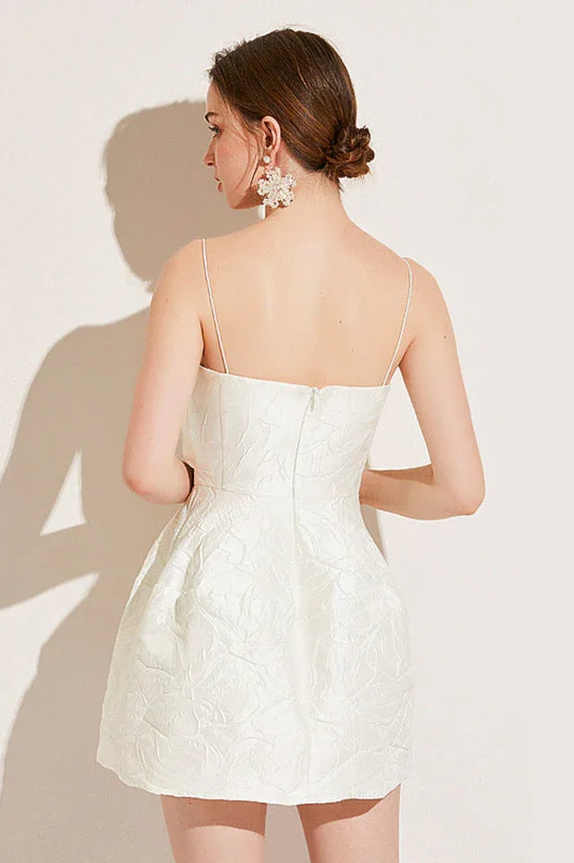 Detail shot of the textured floral pattern on the skirt of a white asymmetrical neckline dress.
