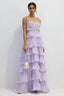 Woman wearing a long, light purple tiered ruffled chiffon dress with a floral applique bodice and tie shoulder straps, holding a pearl clutch.