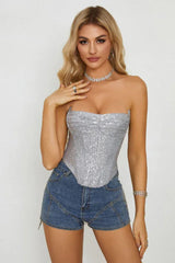 Woman in a silver sequined corset top and denim shorts, posing with hand on chest