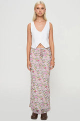 Front view of a woman in a white sleeveless vest and a pink floral maxi skirt.