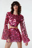 Front view of a woman wearing a pink sequined crop top with bell sleeves and a matching mini skirt with a cut-out detail at the waist.