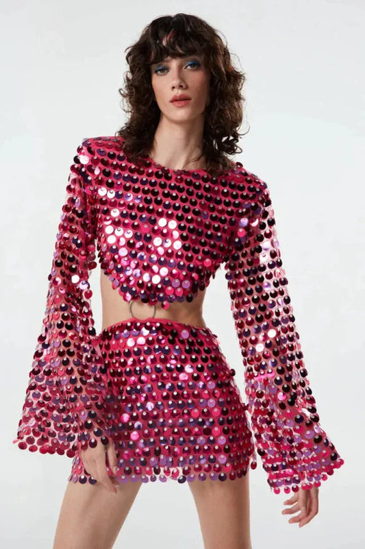 Front view of a woman wearing a pink sequined crop top with bell sleeves and a matching mini skirt with a cut-out detail at the waist.