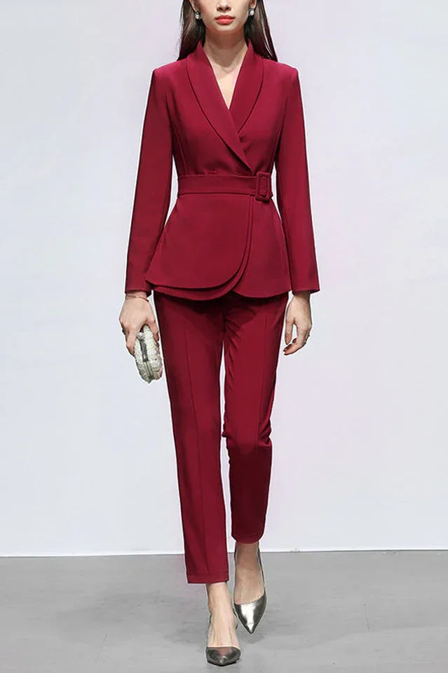 Woman wearing a red belted blazer with matching trousers and silver pointed-toe heels, holding a white clutch.
