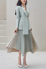 Woman wearing a light blue blazer and asymmetrical pleated skirt, standing with a scarf detail.