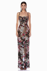 Woman wearing a floor-length black sheer gown with colorful floral appliqués and sequins, featuring spaghetti straps and a straight neckline.