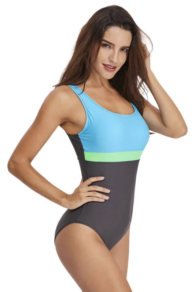 Woman wearing a grey, light blue, and lime green color-blocked one-piece swimsuit, side view.