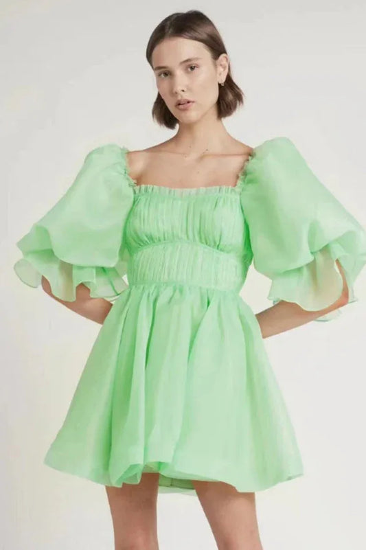 Woman wearing a short, light green organza dress with dramatic puff sleeves and a square neckline.