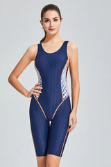 Woman in a navy blue one-piece swimsuit with orange and pink geometric side panels, posing with hand on hip