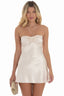 Woman wearing a cream satin halter mini dress with a floral applique on the bust, holding a gold clutch.