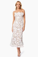 Woman wearing a white strapless midi dress with floral embellishments and a trumpet skirt.
