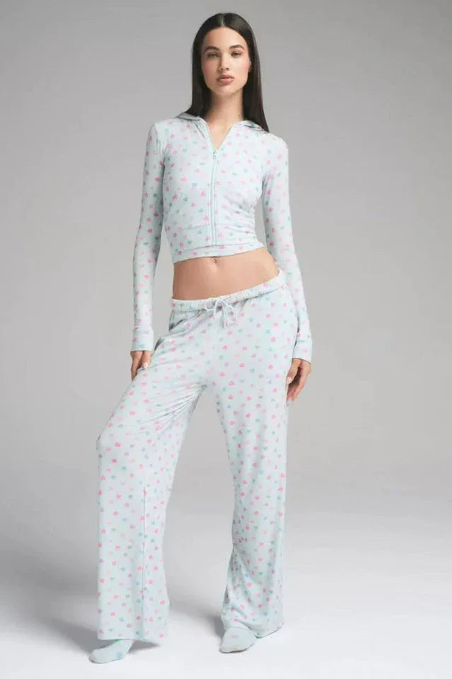 Woman in a light blue cropped hoodie with heart prints, hands in pockets.
