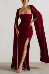 Model posing in a maroon formal dress with a high leg slit and dramatic cape sleeves.