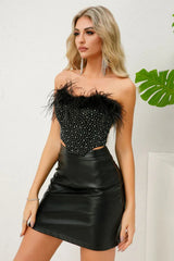 Back view of a woman in a black strapless corset top with feather trim and rhinestone embellishments, and a black faux leather skirt, showing zipper closure.