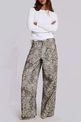 Model wearing wide leg leopard print denim pants and a white long-sleeved shirt, arms crossed.