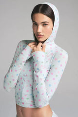 Close-up of a woman wearing a light blue cropped hoodie with heart prints, hands near her neck.